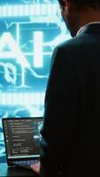 Vertical AI system administrator using laptop device in high tech futuristic workspace. Man working on notebook to automatize tasks using artificial intelligence technology, camera A video