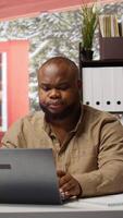 Vertical Entrepreneur sitting at his desk working on laptop with wireless technology for remote job efficiency. Analyzing data and developing strategies, successful telecommuting from home office. Camera B. video