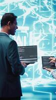 Vertical Team of admins using tablet and laptop to maintenance artificial intelligence neural networks. Teamworking IT staff members using AI system aiding in processing and transmitting information, camera B video