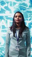 Vertical Portrait of smiling IT specialist standing with arms crossed in front of cutting edge display featuring AI and neural network graphics. Researcher in startup doing advancements in AI field, camera B video
