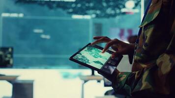 Army soldier reviews targets on a satellite world map to ensure global protection, works on tablet in military command center. Private examines battlefield data for intelligence. Close up. Camera B. video