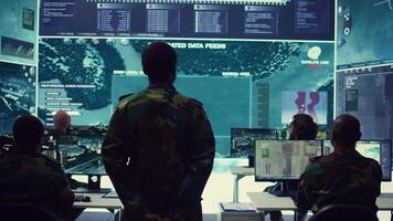Staff sergeant monitoring satellite live imagery on a big screen, gathering information for future military operations. Army officer employs reconnaissance system in command post. Camera B. video