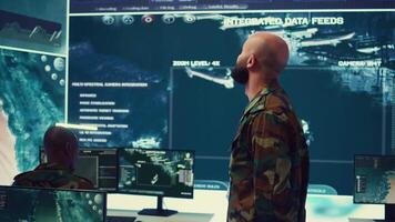 Commander managing cybersecurity measures to protect federal data from enemy breaches, working with his crew from a control center military base. Army officer ensures national safety. Camera B. video
