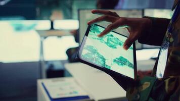 Military IT professional gathers intelligence from world map projection, tablet connected to satellite reconnaissance system to support field troops. Dispatch army command post. Close up. Camera B. video