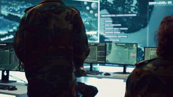 General of the army overseeing special reconnaissance mission in control center, undertake intelligence gathering operations with CCTV footage and a world map on a big screen. Camera A. video