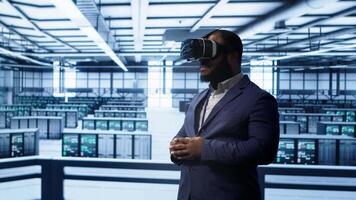 African american developer immersed in virtual reality at data center, doing units maintenance. Technician using VR headset to optimize servers performance, checking operations, camera A video