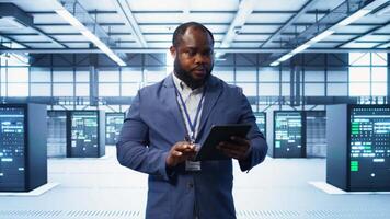 IT technician walking in data center, overseeing server operations using tablet. Expert ensuring optimal performance and data integrity in server hub using digital device, camera B video