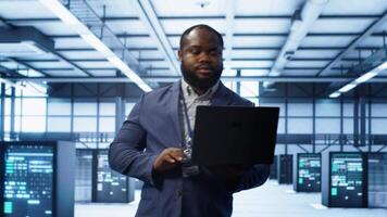 IT engineer working on laptop in modern data center, overseeing server operations, system maintenance,and cybersecurity protocols, ensuring optimal performance and data integrity, camera A video