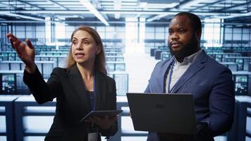 Teamworking colleagues doing checkup, inputting data on laptop of needed server hub fixes. Coworkers working together in data center housing advanced storage infrastructure, camera B video