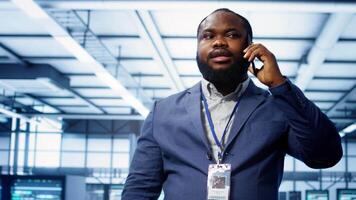 Close up shot of programmer in data center talking in phone call, doing inspection. On field IT specialist talking with manager in server hub during telephone call, monitoring mainframes, camera B video
