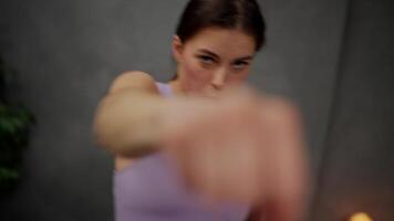 Close up dynamic portrait of a confident brunette girl in a purple top who practices boxing strikes in a modern apartment while playing sports at home video