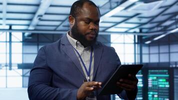 IT technician walking in data center, overseeing server operations using tablet. Expert ensuring optimal performance and data integrity in server hub using digital device, camera A video