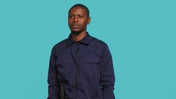 Security guard does surveillance for various organizations and venues, ensuring protection of property and personnel, studio background. Portrait of intimidating man in uniform crossing arms, camera A video