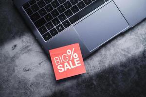 Laptop with a red adhesive note with big sale on it. Discounts, online shopping. Desktop view with copy space. photo