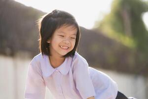 Portrait of smiling child in green park. A good-humored little girl with a sweet, bright smile. In the evenings after school, summer or spring, children are happy and cheerful. Kid wear school uniform photo