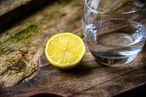 A glass of water and a ceramic plate with fruit, lemon, lime on a wooden table in a rustic kitchen. photo