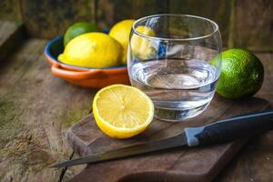 A glass of water and a ceramic plate with fruit, lemon, lime on a wooden table in a rustic kitchen. photo