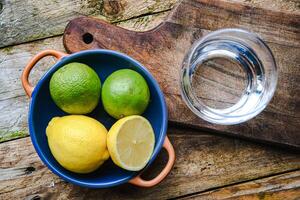 A glass of water and a ceramic plate with fruit, lemon, lime on a wooden table in a rustic kitchen. photo