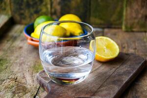 A glass of water and a ceramic plate with fruit, lemon, lime on a wooden table in a rustic kitchen. photo