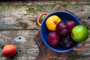 plums, lime, tangerine in a ceramic bowl and apricot on a wooden table photo