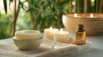 A moisturizer tub is placed on a plush white towel next to a bowl of aromatic essential oils and a few lit candles. photo
