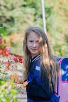 Back to school, portrait of a little girl from primary school outdoors, enjoying flowers in a flowerbed and looking at the camera with a smile, student dressed in dark blue uniform photo