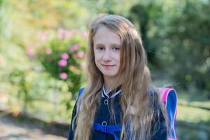 Back to school, portrait of a little girl from primary school outdoors, enjoying flowers in a flowerbed and looking at the camera with a smile, student dressed in dark blue uniform photo