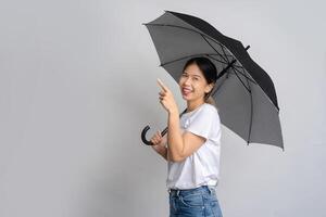 Happy Asian woman standing holding a umbrella and pointing at copy space on gray background. photo