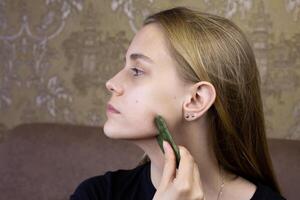Profile of European girl who does facial massage using gua sha scraper to take care of health of skin and body, procedure for cleaning face and stretching wrinkles using special scraper photo