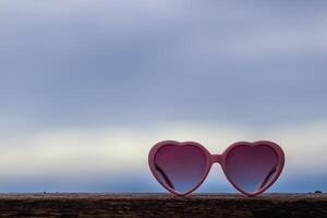 Pink heart shaped glasses are placed on wooden table and there is copy space for adding love messages. heart shaped symbol background says I love you and the heart shape is also a symbol of friendship photo