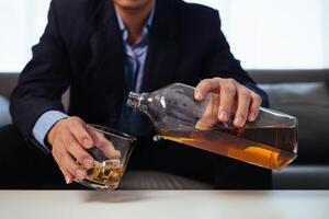 businessman sits and holds glass of liquor in his hand to drink relieve stress after experiencing problems in business. businessman drinking alcohol relieve stress from failed business venture. photo