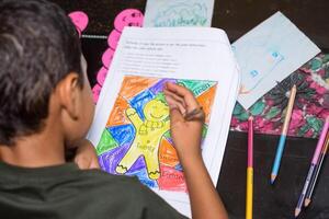 Smart Indian little boy drawing with colourful pencils kit of various colours during the summer vacations, Cute Indian Kid Sketching colourful drawing on wooden table photo