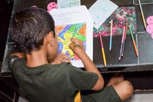 Smart Indian little boy drawing with colourful pencils kit of various colours during the summer vacations, Cute Indian Kid Sketching colourful drawing on wooden table photo
