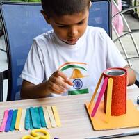 Smart Indian little boy performing best out of waste activity with different colourful objects during the summer vacations, Cute Indian Kid doing best our of waste activity at home on wooden table photo