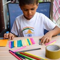 Smart Indian little boy performing best out of waste activity with different colourful objects during the summer vacations, Cute Indian Kid doing best our of waste activity at home on wooden table photo