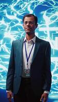 Vertical Smiling technician in startup stands with arms crossed, exuding professionalism and expertise. Portrait of cheerful Indian IT expert working in futuristic artificial intelligence workspace, camera B video