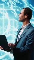 Vertical IT expert solving tasks on laptop device, running artificial intelligence programming scripts. Indian man using notebook to write lines of code for AI applications development, camera A video