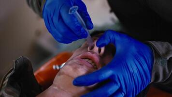 Close-up a confident male medic with his own hands in blue medical rubber gloves inserts a breathing tube for artificial respiration into the nose of a doll of an injured soldier during a first aid video