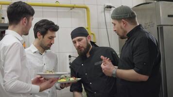 Two chefs in black uniforms together with waiters in white shirts communicate about the prepared dishes and solve their problems while working in the kitchen and restaurant. Cooks and waiters solve video