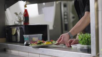 A cook in a black uniform puts the finished salad dish on the serving table and notifies the waiter about this using a bell in a restaurant video