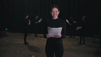 Portrait of a confident brunette actor girl in a black suit with a pile of script papers and text in her hands in a group of actors who are preparing to perform on stage in the theater video