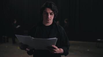 Portrait of a confident Happy man with medium-length brunette hair in a black suit an actor who holds a piece of paper in each of his hands and reads the text of your character and the script of the video