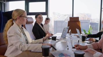 Confident brunette girl in business clothes holds a small infant baby in her arms while taking part in a business meeting at a table in a modern office with large windows video