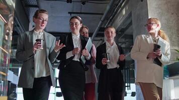 Front view of a group of confident businesswoman colleagues walking along the corridor in the office and talking about their current issue and affair. Group of confident businesswoman colleagues in video