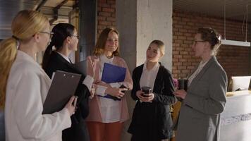 Side view of a group of confident businesswomen in business clothes communicating during a short break in a modern office video