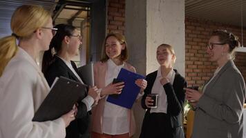 A group of confident business girls in glasses and business suits stand in a semicircle and chat during a break from work in a modern office video