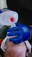 Vertical close-up of a confident man in blue medical gloves pumping air and performing artificial respiration on a man who is lying on a couch in a small medical room video