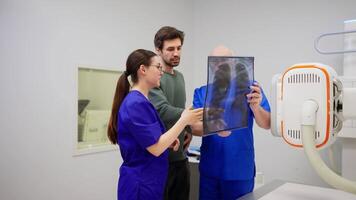 A brunette man with stubble in a green jacket communicates with a girl and a male doctor in a blue uniform after performing fluorography in front of an image of his own chest on a special transparent video