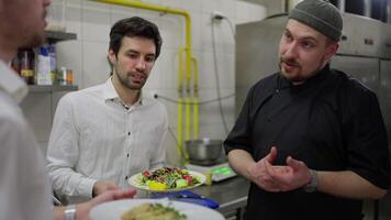 Close up over the shoulder of a confident male chef in a black uniform talking with waiters about teamwork in the kitchen in a restaurant. A professional chef is dissatisfied with the work of waiters video