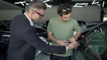 A confident middle-aged man in a business suit a manager at a car dealership holds a tablet in his hands and communicates with a young client about a car video